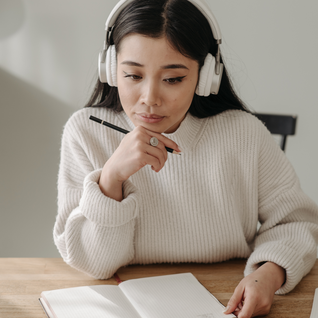 Persona estudiando y tomando apuntes con auriculares puestos, simbolizando concentración y aprendizaje.