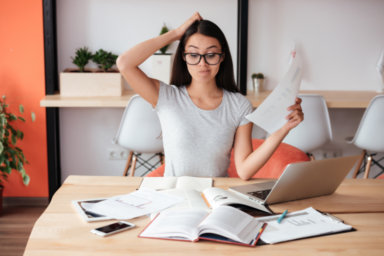 Estudiante confundida revisando documentos mientras estudia con su computadora