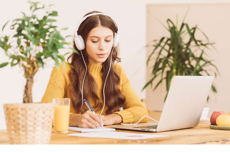 Estudiante tomando notas mientras escucha una clase en línea con audífonos